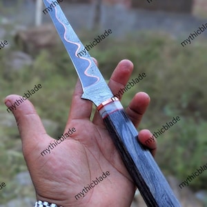 May include: A Damascus steel knife with a wavy pattern on the blade and a dark wooden handle. The blade has a copper-colored accent. The knife is held in a hand, with the text "mythicblade" repeated around the image.