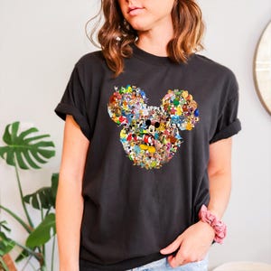 May include: Dark grey t-shirt with a Mickey Mouse head design made up of numerous Disney characters. The graphic is in the centre of the shirt. The t-shirt has short sleeves and a relaxed fit, suitable for casual wear.