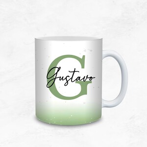 May include: White ceramic mug with a green ombre design. The letter "G" and the name "Gustavo" are displayed in a stylish font. The mug has a white handle and a light green gradient at the bottom.