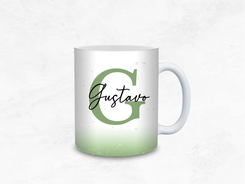 May include: White ceramic mug with a green ombre design. The letter "G" and the name "Gustavo" are displayed in a stylish font. The mug has a white handle and a light green gradient at the bottom.
