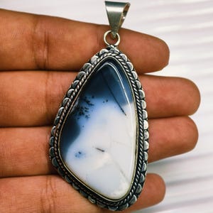 May include: A teardrop-shaped pendant featuring a smooth, polished white and dark blue dendritic agate stone. The gemstone is encased in a decorative silver-toned metal setting with a braided rope border and a triangular bail at the top.