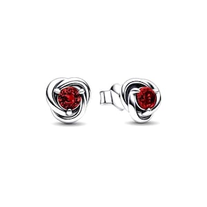 May include: A pair of silver stud earrings. Each earring features a round, vibrant red gemstone set in a swirling, knot-like design. The earrings are displayed against a white background, highlighting their intricate details and color.