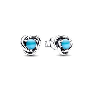 May include: A pair of silver stud earrings. Each earring has a light blue, round gemstone set in a swirling, knot-like design. The earrings are presented against a white background.