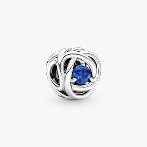 Puede incluir: Un charm de plata con un diseño tejido, con una gema azul vibrante en el centro. El charm es redondo y tiene un acabado pulido, creando un contraste llamativo entre el metal y la gema. Esta pieza de joyería es adecuada para pulseras y collares.