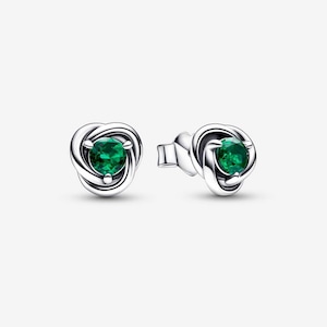 Puede incluir: Un par de pendientes de botón plateados. Cada pendiente presenta una piedra preciosa verde redonda y vibrante engastada en un diseño arremolinado en forma de nudo. Los pendientes se muestran sobre un fondo blanco.