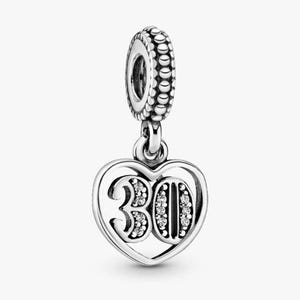 Op de afbeelding: Een zilveren bedel met een hartvormige hanger met het nummer "30". Het nummer is versierd met kleine, sprankelende steentjes. De bedel heeft een kralen bovenkant en is ontworpen om aan een armband of ketting te worden toegevoegd.