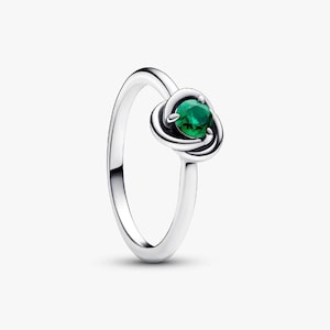 Könnte beinhalten: Ein silberner Ring mit einem Knoten-Design, der einen runden, smaragdgrünen Edelstein hält. Der Ring hat eine polierte Oberfläche und ein schlichtes Band. Der Edelstein ist der Mittelpunkt, eingebettet in den Knoten.