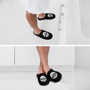 Pode incluir: Chinelos pretos de biqueira aberta com um design circular que diz "YOUR DESIGN HERE" em branco. Os chinelos s&atilde;o mostrados nos p&eacute;s de uma pessoa, sugerindo conforto e relaxamento. Os chinelos s&atilde;o de cor preta lisa.