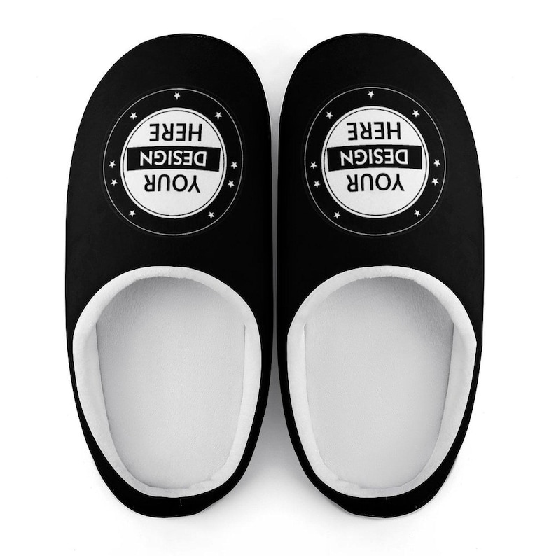 Pode incluir: Um par de chinelos pretos com interior branco. Cada chinelo apresenta um design circular com o texto "YOUR DESIGN HERE" em branco. Estes chinelos de interior est&atilde;o sobre um fundo branco.