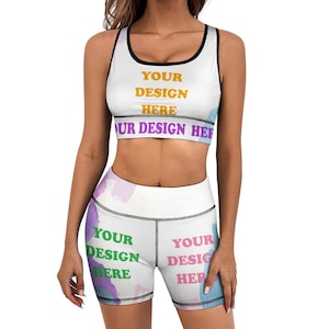 May include: White sports bra and matching shorts set with black trim. The bra and shorts feature the text "YOUR DESIGN HERE" in various colors. The shorts have a watercolor-style design in shades of purple, blue, and green.