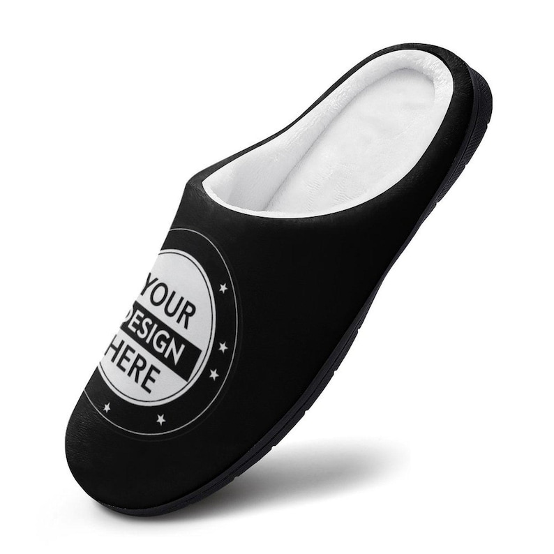 Pode incluir: Chinelo preto com interior branco e fofo. O chinelo apresenta um emblema redondo com o texto "YOUR DESIGN HERE" num ret&acirc;ngulo preto, rodeado por um c&iacute;rculo branco e estrelas. Desenhado para uso interno.