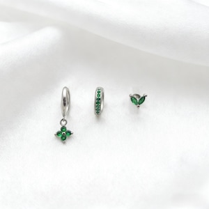 May include: A set of three silver earrings with green gemstones. One earring is a small hoop with green stones, another is a stud with two green leaf-shaped stones, and the third is a dangle earring with a four-leaf clover design.