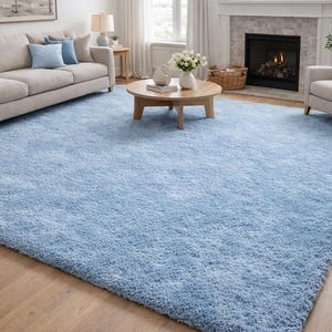 Könnte beinhalten: Ein großer, rechteckiger, hellblauer Shag-Teppich dominiert einen Wohnraum. Der Teppich liegt auf einem Holzboden, im Hintergrund ein beiges Sofa mit blauen Kissen. Ein runder Holztisch und ein Kamin sind ebenfalls zu sehen.