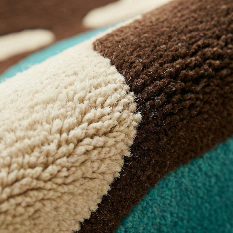 Puede incluir: Primer plano de una secci&oacute;n de una alfombra con un pelo rizado texturizado. La alfombra presenta un patr&oacute;n de rayas alternas en crema, marr&oacute;n y turquesa. Las fibras son gruesas y crean una apariencia suave y afelpada.