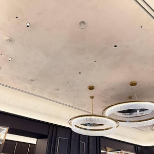 May include: A ceiling featuring recessed lighting, speakers, and multiple circular chandeliers with gold frames and crystal detailing. The ceiling has a light beige, textured finish. The chandeliers are the main feature, contributing a sense of sophistication.