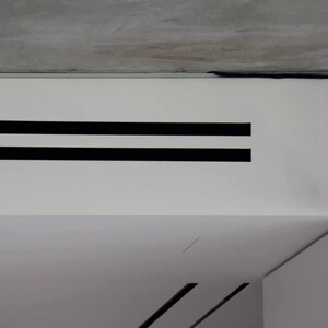 Puede incluir: Toma interior que muestra una pared blanca con dos franjas negras horizontales. Un cable negro recorre el techo y una l&aacute;mpara negra cuelga del techo. El techo es de hormig&oacute;n.