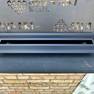 May include: A black metal vent cover with a rectangular design. The vent cover has a series of horizontal lines and a recessed centre. The background features the text "SAVA ART METAL".