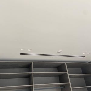 Puede incluir: Un mueble de almacenamiento empotrado gris con estantes abiertos y m&uacute;ltiples compartimentos. La unidad est&aacute; debajo de un techo blanco con iluminaci&oacute;n empotrada y un detector de humo. El dise&ntilde;o es moderno y minimalista.