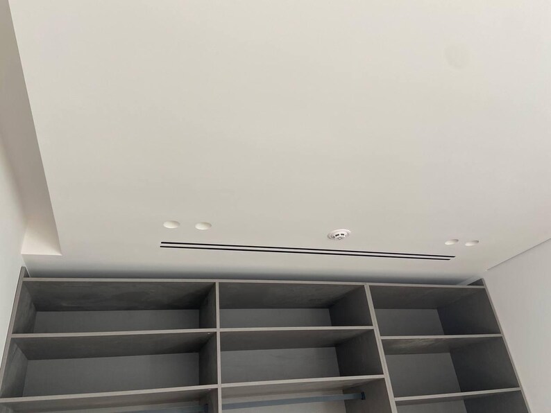 Puede incluir: Un mueble de almacenamiento empotrado gris con estantes abiertos y m&uacute;ltiples compartimentos. La unidad est&aacute; debajo de un techo blanco con iluminaci&oacute;n empotrada y un detector de humo. El dise&ntilde;o es moderno y minimalista.