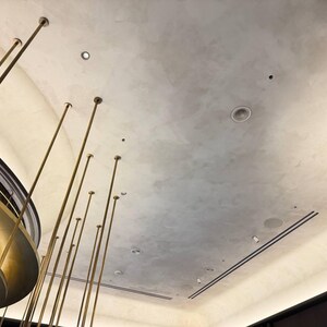May include: An upward view of a ceiling with a textured, light grey finish. Several thin, gold-coloured poles extend upwards from the bottom of the frame. Recessed lighting fixtures and a decorative gold-coloured structure are also visible.