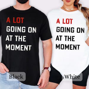 May include: Black and white t-shirts with the text "A LOT GOING ON AT THE MOMENT" in a distressed font. The black shirt has a "Black" label, and the white shirt has a "White" label.
