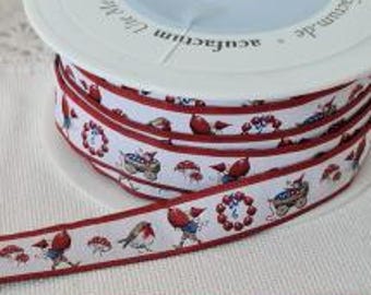 Könnte beinhalten: Eine Spule mit weißem Band mit einem sich wiederholenden Muster aus roten Vögeln, Pilzen und Beerenkränzen. Das Band hat einen dünnen roten Rand und ist teilweise abgerollt. Die Spule hat Text auf Deutsch.