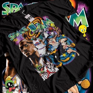 May include: Black t-shirt featuring a colorful graphic from the movie Space Jam. The design includes Michael Jordan, Bugs Bunny, and other Looney Tunes characters. The text "SPACE JAM" is prominently displayed in a vibrant, multi-colored font.