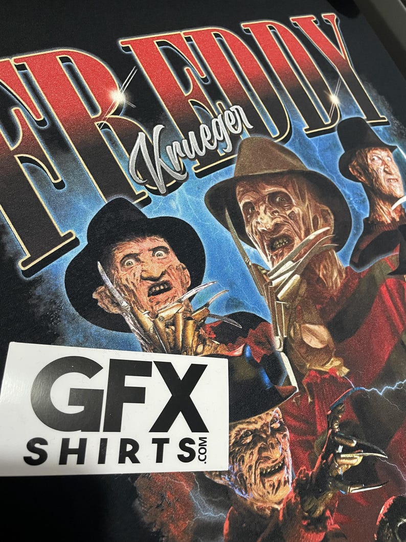 May include: Black t-shirt with a graphic of Freddy Krueger from the Nightmare on Elm Street films. The design includes multiple images of Krueger with his signature hat and bladed glove. The text "FREDDY Krueger" is printed across the top. The shirt also has a sticker that says "GFX SHIRTS.com".