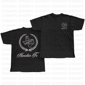May include: Black t-shirts with white graphics. One shirt features a Texas outline with a building design and the text "Houston Tx" inside a laurel wreath. The other shirt has a similar design on the front.