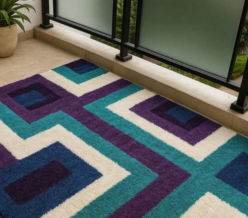 Puede incluir: Una alfombra rectangular con un patr&oacute;n geom&eacute;trico en tonos de azul, turquesa, morado y blanco. La alfombra presenta un dise&ntilde;o repetitivo de cuadrados y zigzags, creando una est&eacute;tica moderna. La alfombra est&aacute; hecha de un material suave y texturizado.