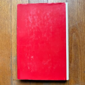 Puede incluir: Un libro con una cubierta roja brillante y un lomo blanco. El libro est&aacute; sobre una superficie de madera. La cubierta tiene un aspecto ligeramente desgastado.