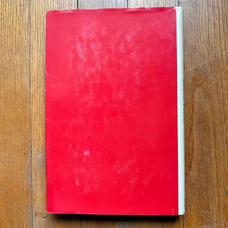 Puede incluir: Un libro con una cubierta roja brillante y un lomo blanco. El libro est&aacute; sobre una superficie de madera. La cubierta tiene un aspecto ligeramente desgastado.