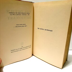 May include: Open book titled "The Devil's Dictionary" with text on the left page including the publisher's name and address, and the printing date of August 1948. The right page displays the title. The book has aged, off-white pages.