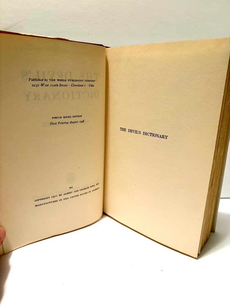 May include: Open book titled "The Devil's Dictionary" with text on the left page including the publisher's name and address, and the printing date of August 1948. The right page displays the title. The book has aged, off-white pages.