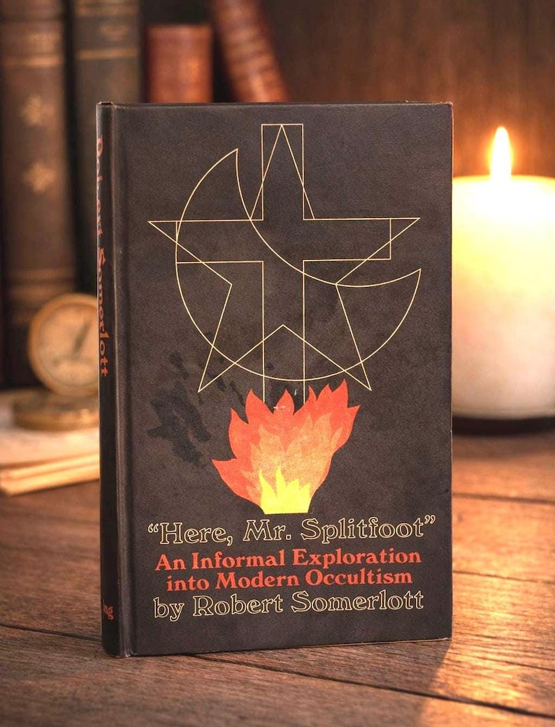 Puede incluir: Un libro de tapa dura negro con dise&ntilde;os geom&eacute;tricos dorados y una ilustraci&oacute;n de llama. El t&iacute;tulo es "Here, Mr. Splitfoot" de Robert Somerlott. El libro trata sobre ocultismo moderno.
