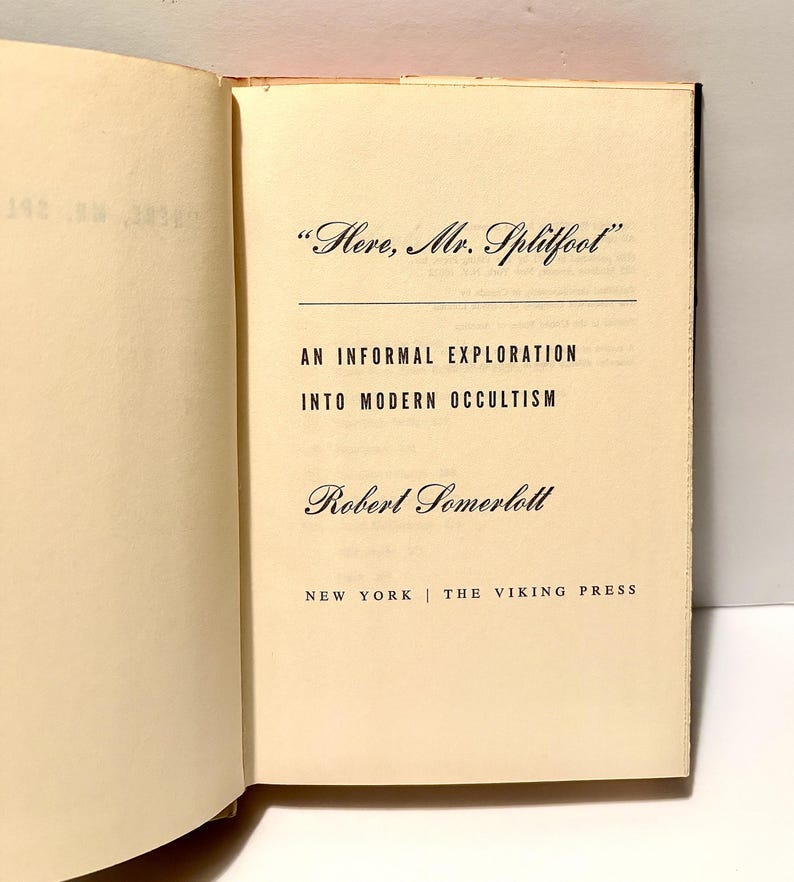 Puede incluir: Libro abierto con el t&iacute;tulo "Here, Mr. Splitfoot" y el subt&iacute;tulo "An Informal Exploration Into Modern Occultism". El nombre del autor, Robert Somerlott, est&aacute; debajo del t&iacute;tulo. Publicado por The Viking Press en Nueva York.
