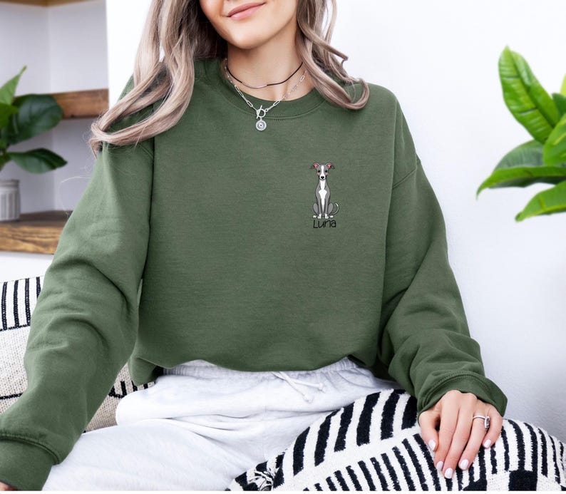 K&ouml;nnte beinhalten: Ein olivgr&uuml;nes Sweatshirt mit einer gestickten Illustration eines Windhundes und dem Namen "Luna". Der Hund hat ein rotes Halsband. Das Sweatshirt hat einen Rundhalsausschnitt und lange &Auml;rmel. Das Design befindet sich auf der linken Brust.