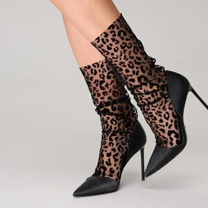 Pode incluir: Saltos agulha pretos combinados com meias de tornozelo transparentes com estampa de leopardo. As meias t&ecirc;m uma borda com babados. Os sapatos t&ecirc;m um design pontudo.