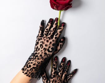 Puede incluir: Guantes negros transparentes con estampado de leopardo sosteniendo una rosa roja con tallo verde. Fondo blanco. Un accesorio elegante para eventos especiales.