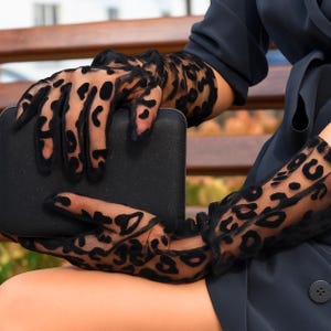 Pode incluir: Luvas pretas transparentes com um design de estampa de leopardo. As luvas longas cobrem os antebra&ccedil;os e s&atilde;o combinadas com uma clutch retangular preta. O design apresenta manchas escuras em um fundo transparente.