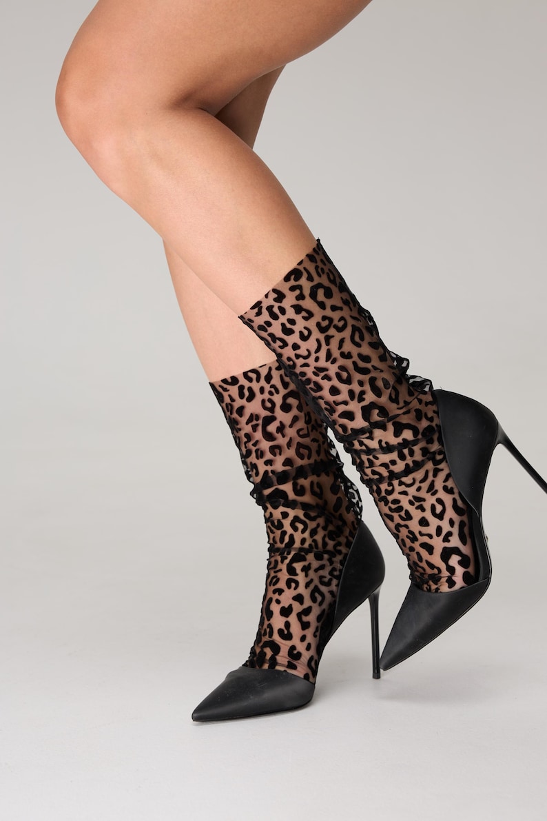 Pode incluir: Saltos agulha pretos combinados com meias de tornozelo transparentes com estampa de leopardo. As meias t&ecirc;m uma borda com babados. Os sapatos t&ecirc;m um design pontudo.