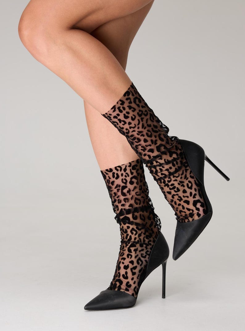 Pode incluir: Sapatos pretos de salto alto com bico fino. Os sapatos s&atilde;o combinados com meias pretas transparentes com estampa de leopardo. As meias s&atilde;o franzidas nos tornozelos. O fundo &eacute; liso.