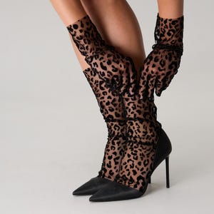 Pode incluir: Sapatos pretos de salto alto com bico fino. A imagem tamb&eacute;m mostra luvas e meias pretas transparentes com estampa de leopardo. O fundo &eacute; branco liso.