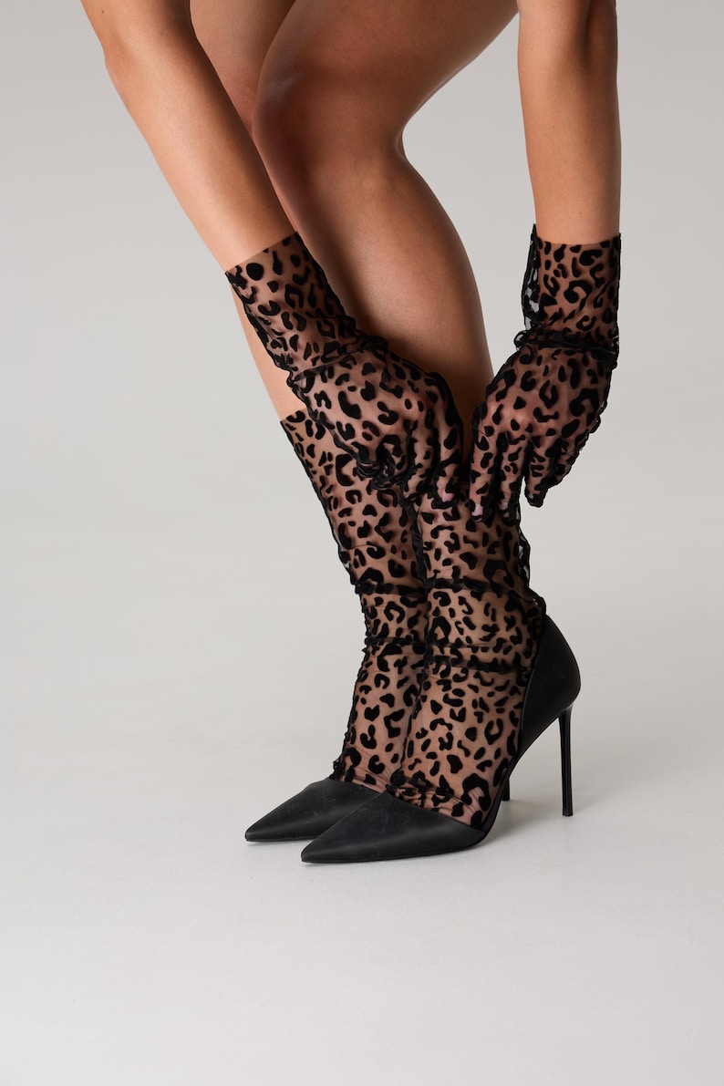 Pode incluir: Sapatos pretos de salto alto com bico fino. A imagem tamb&eacute;m mostra luvas e meias pretas transparentes com estampa de leopardo. O fundo &eacute; branco liso.