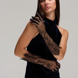 May include: Black lace opera gloves with floral patterns. The gloves extend to the upper arm and are made of a delicate, sheer fabric. The gloves are worn with a dark blue velvet halter dress.