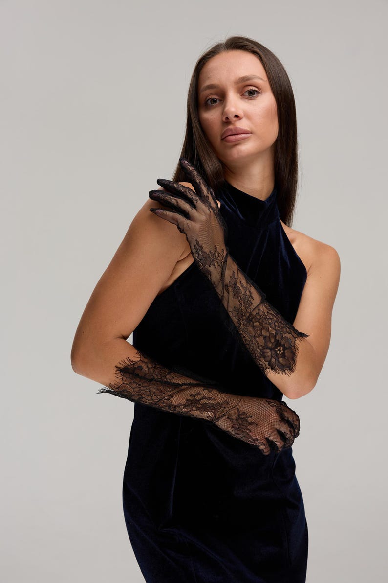 May include: Black lace opera gloves with floral patterns. The gloves extend to the upper arm and are made of a delicate, sheer fabric. The gloves are worn with a dark blue velvet halter dress.