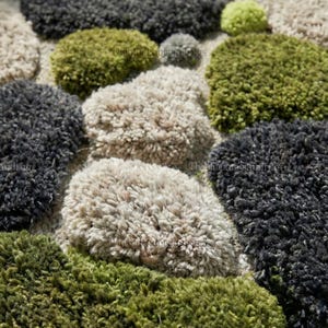 Modern hand-tufted beige wool rug with pebble pattern on balcony; 3D textured abstract carpet in gray, black, moss green.