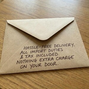 Brown kraft envelope on a wood table, featuring a handwritten note about hassle-free delivery and duties included.