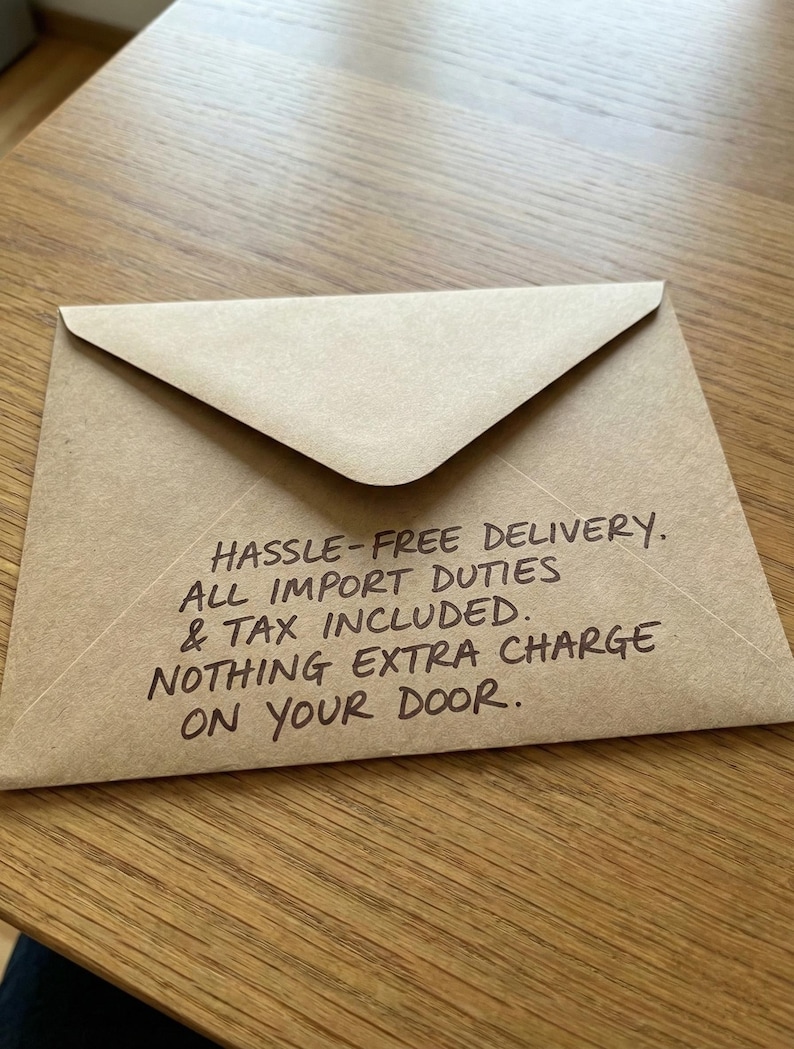 Brown kraft envelope on a wood table, featuring a handwritten note about hassle-free delivery and duties included.