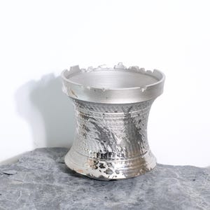 Peut inclure: Une figurine d'un fou d'échecs de couleur argentée. La pièce d'échecs a une surface texturée et rugueuse et un sommet crénelé. Le fou est exposé sur une surface grise et texturée sur fond blanc. La pièce d'échecs est un objet décoratif.